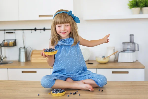 Sevimli küçük kız mavi elbiseli bir el ve kapalı gözler pastada bir masada oturur