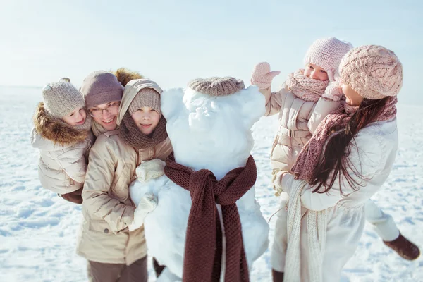 Ritratto di famiglia felice vicino a un pupazzo di neve in inverno — Foto Stock