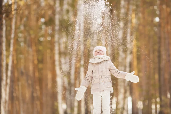 Portrait de petite fille vêtue d'un vêtement beige jette une neige dans un parc en hiver — Photo