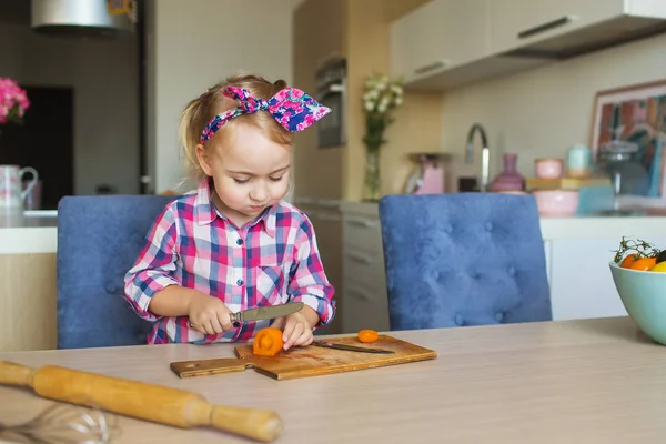 La bella bambina taglia e mangia un vegetale su una cucina — Foto Stock