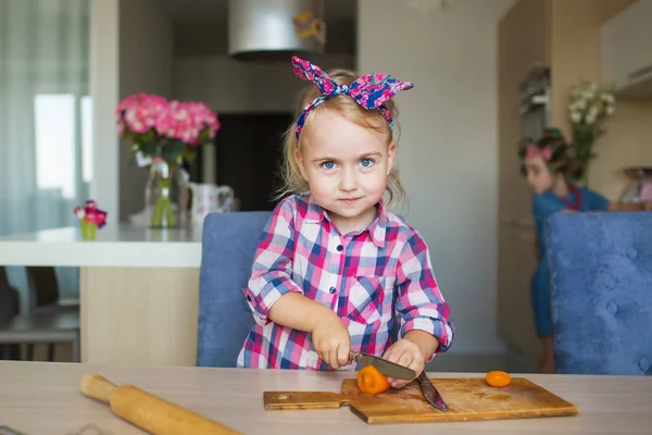 La bella bambina taglia un vegetale su un'asse su una cucina — Foto Stock