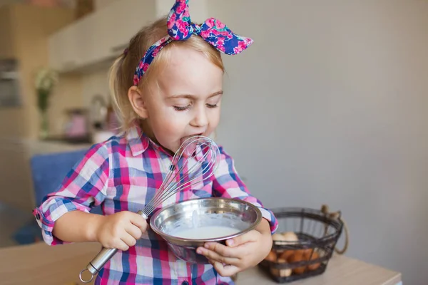 Ritratto di bella bambina in camicia a scacchi si solleva e lecca una crema a casa — Foto Stock