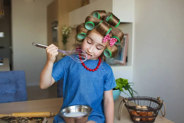 Ragazzina divertente in abito blu e con bigodini prova una crema su una cucina — Foto Stock