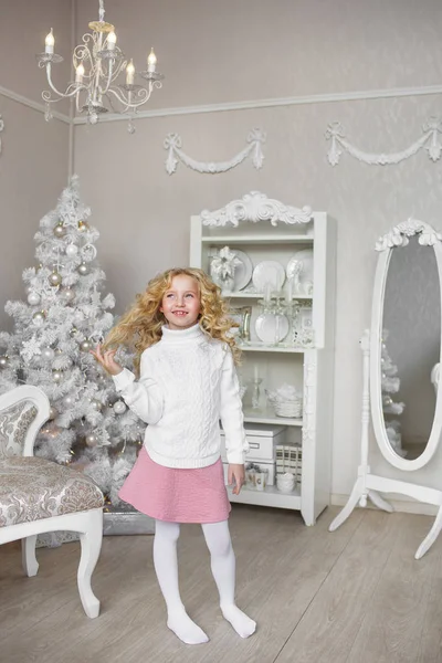 Pretty little girl stands and touches her hair in a light new year decoration studio — Stock Photo, Image