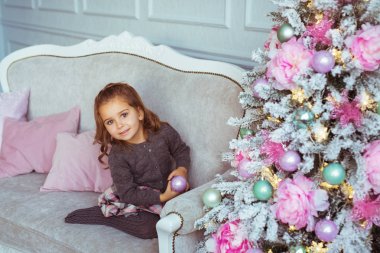 Sevimli küçük kız Noel ağacı yakınındaki bir kanepede oturuyor