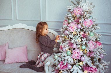 Küçük kız kanepede oturur ve bir ağaç oyuncaklar Noel ağacı evde dokunur