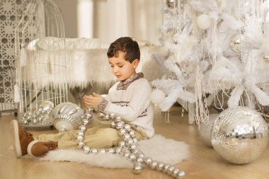 Sevimli küçük çocuk bir katta oturur ve Noel ağacı yakınındaki bir büyük cam oyuncakla oynar