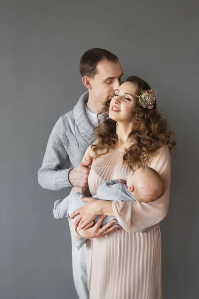 Familia de adultos jóvenes con un bebé sobre un fondo gris —  Fotos de Stock