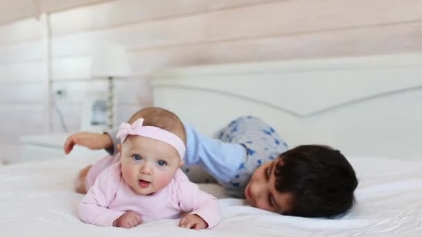 Mignon frère joue avec sa petite sœur sur un lit à la maison — Video