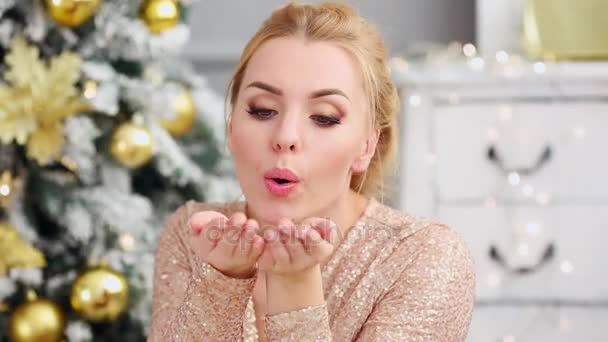 Schöne junge Frau bläst ein Konfetti aus den Händen in der Nähe des Weihnachtsbaums — Stockvideo