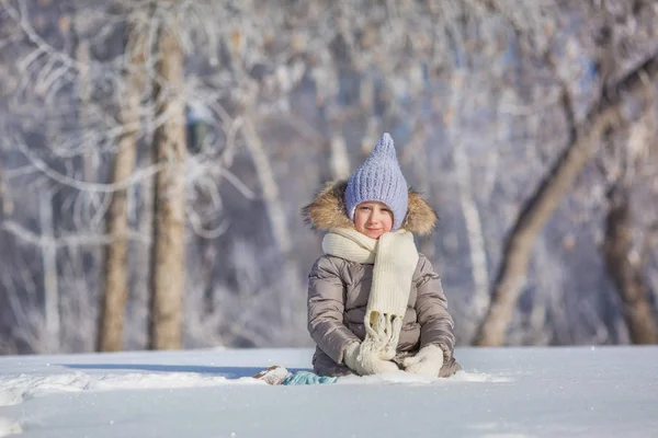 Маленькая девочка в теплой одежде зимой сидит в снегу — стоковое фото