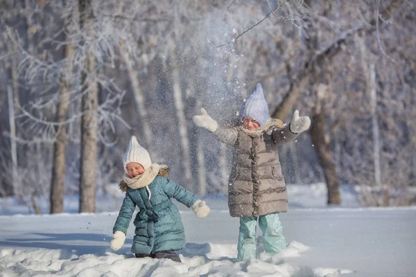 Дві маленькі сестри грають і кидають сніг взимку — стокове фото