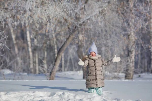 Bambina in giacca grigia gioca con la neve nella foresta invernale — Foto Stock