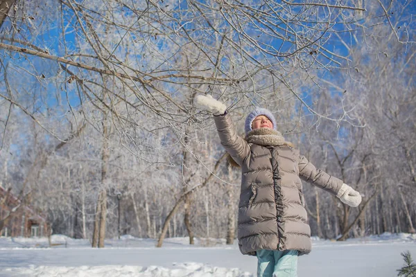 Маленькая девочка в серой куртке играет в зимнем лесу в солнечный день — стоковое фото