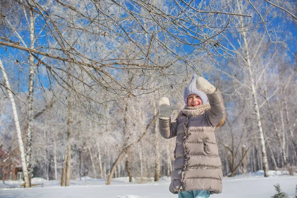 Маленькая девочка играет с деревом в зимнем парке в солнечный день — стоковое фото