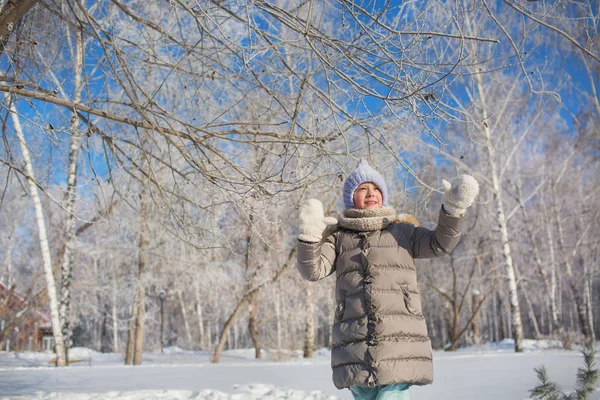 Маленькая девочка в серой куртке гуляет в зимнем парке в солнечный день — стоковое фото