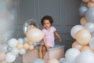 Zenci küçük kız oturur ve bir stüdyoda renkli balonlar ile çalış