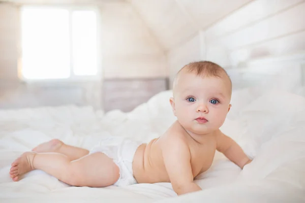 Pequeno bebê em uma fralda encontra-se em uma cama branca no quarto — Fotografia de Stock