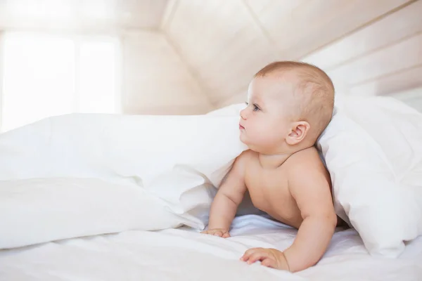 Pequeño bebé mira hacia un lado desde una manta en una cama blanca — Foto de Stock