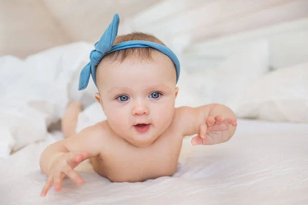 Retrato de bebê sorridente com um diadema azul brinca em uma cama — Fotografia de Stock