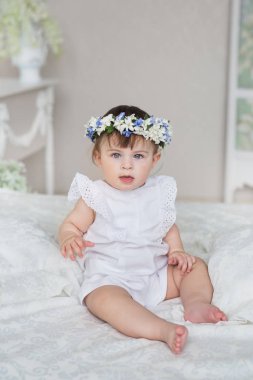 Sevimli küçük kız beyaz bir elbise ve bir diadem üzerinde bir kafa ile bir yatakta oturur