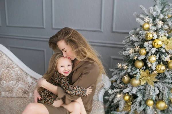 Jeune mère embrasse sa petite fille sur un canapé à Noël — Photo