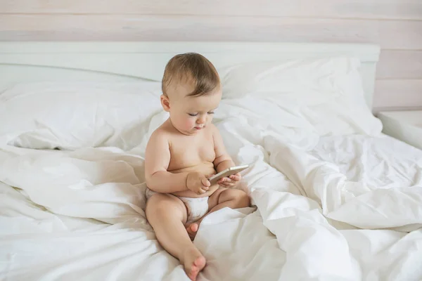 Küçük bebek bir çalış bir yatakta bir akıllı telefon ile memnun etmektedir — Stok fotoğraf