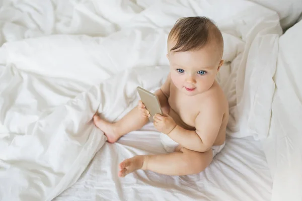 Felülnézet: Kis baba ül az ágyon egy smartphone Stock Kép
