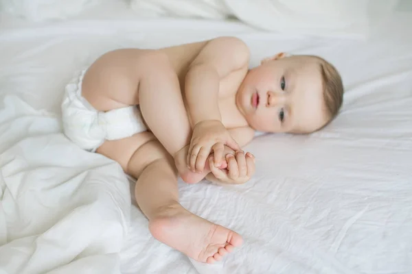 Kaukázusi kis baba megérinti a lábát egy ágyon Stock Kép