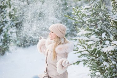 Sevimli kız bir bej ceketi giyen oturur ve bir kış günü kar bir Ladin yakınındaki yukarı atar