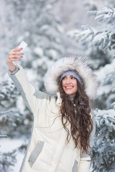 Портрет улыбающейся молодой женщины делает селфи в зимнем лесу — стоковое фото