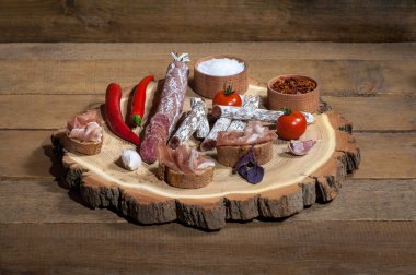 Lezzetli yemekler kırmızı biber, kiraz, tütsülenmiş sosis, tahıl ekmeği, jamon, sarımsak, kurutulmuş domates, fesleğen ahşap arka plan üzerinde ahşap plaka üzerinde.