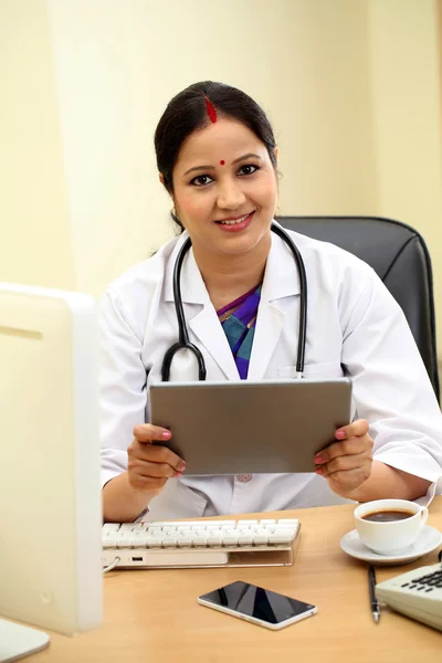 Traditional female doctor holding tablet computer at clinic desk