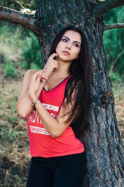 Genç güzel esmer model park arka plan ağaç karşı spor görüntüsünü poz