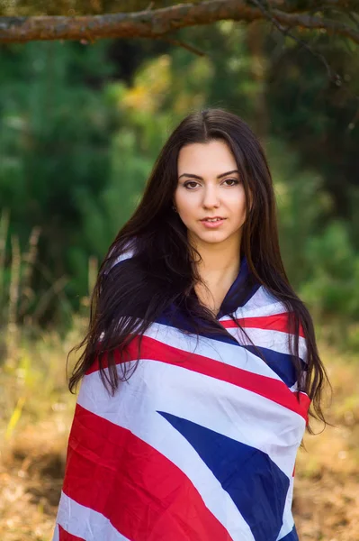 Jovem menina bonita morena posando com uma bandeira britânica no parque de outono — Fotografia de Stock