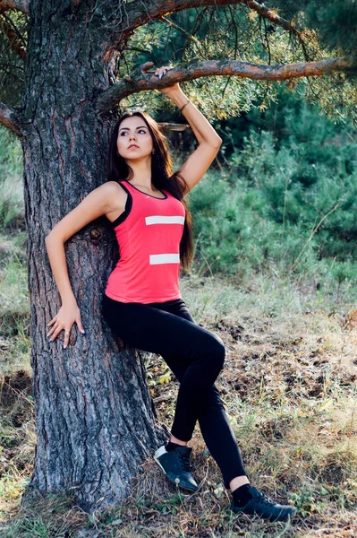 Молодая красивая брюнетка модель позирует в спортивном образе парка на фоне деревьев — стоковое фото