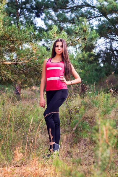 Молодая красивая брюнетка модель позирует в спортивном образе парка на фоне деревьев — стоковое фото