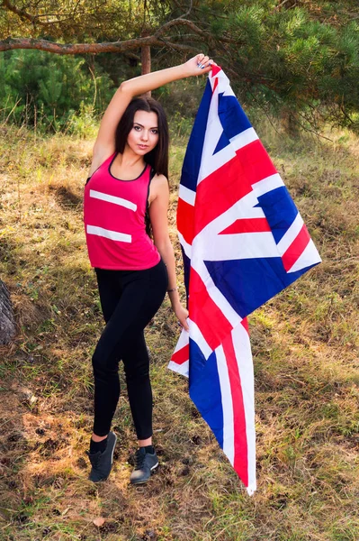 Jovem menina bonita morena posando com uma bandeira britânica no parque de outono — Fotografia de Stock