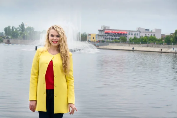 Blonde in een gele jurk tegen de achtergrond fontein — Stockfoto
