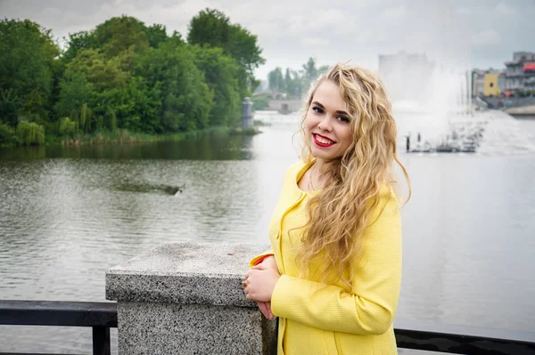 Blonde in een gele jurk tegen de achtergrond fontein — Stockfoto