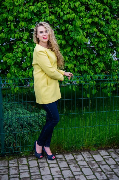 Atrakcyjna blondynka w żółtym fartuchu emocjonalnie pozowanie w parku — Zdjęcie stockowe