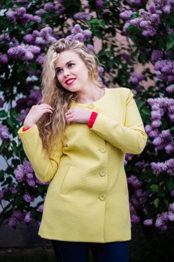 Sarı montlu sarışın kız baharda çiçek açan leylaklar fonunda standları
