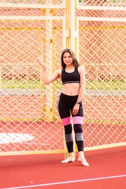 Genç güzel sporcu Stadı nda. Büyüme portre sarı bir çit. Çitin arkasında elini tutar.