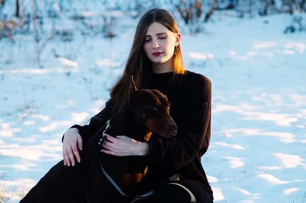 Mooi meisje lopen in een winter park met haar hond Dobermann-RAS — Stockfoto