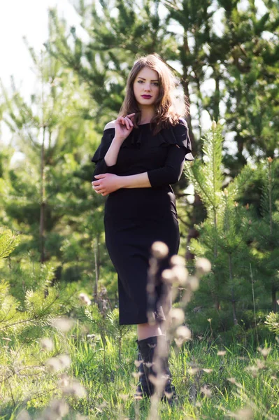 Fashion model in black dress in the summer dressed in a black dress. Against the background of the trees.