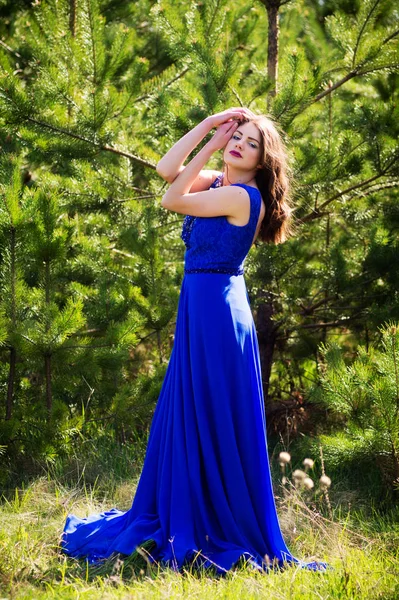 Beautiful fashion model in a dress in a green park in the summer. Holds his hands around his face.