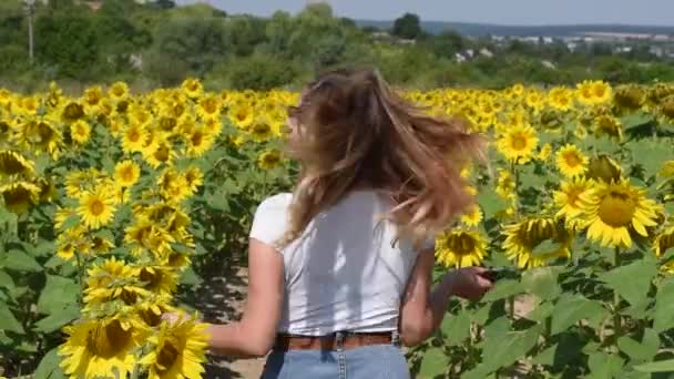 Schöne junge Mädchen in einem weißen T-Shirt dreht sich in einem Sonnenblumenfeld — Stockvideo