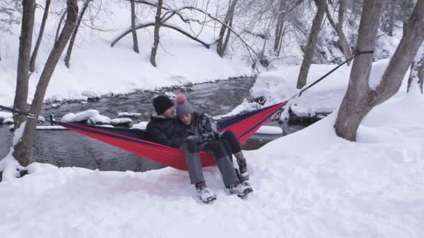 在犹他州的一条河边 一对情侣坐在吊床上 在外面的雪地里摇曳着 拥抱在一起 — 图库视频影像