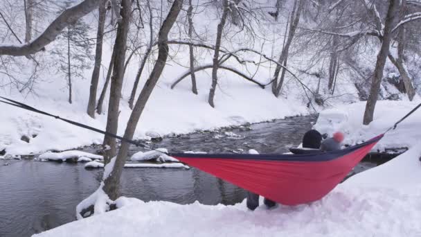 Pareja Sentada Hamaca Atada Afuera Nieve Por Río Mientras Balancean — Vídeos de Stock