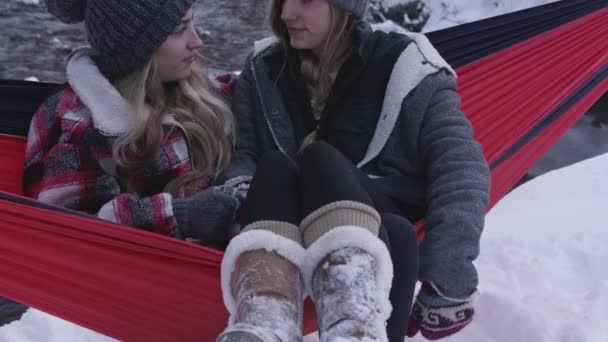 雪が峡谷の川によって風景をカバーするように一緒に冬にハンモックに座って女性にパンニング — ストック動画
